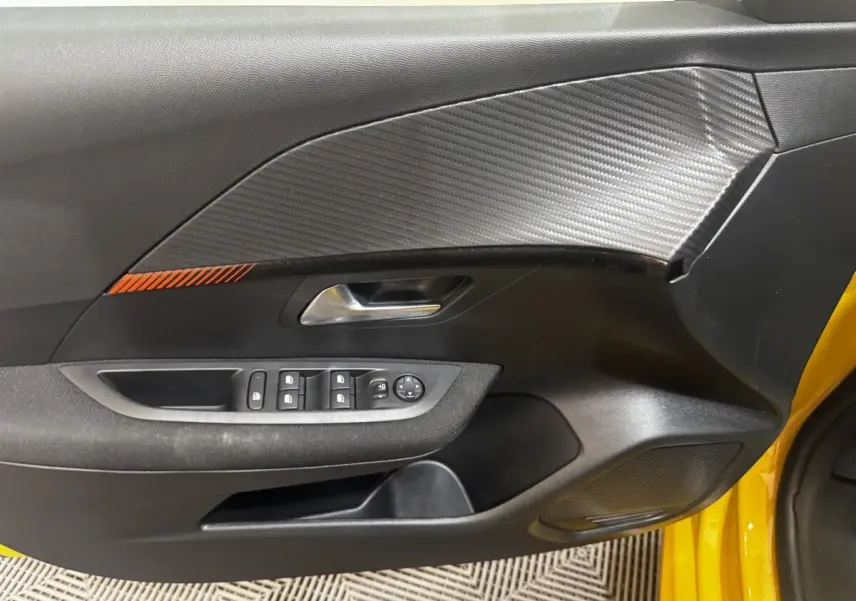 Vue intérieure côté conducteur de la porte noire avec insert effet carbone et détail orange sur Peugeot 208 jaune 2023.