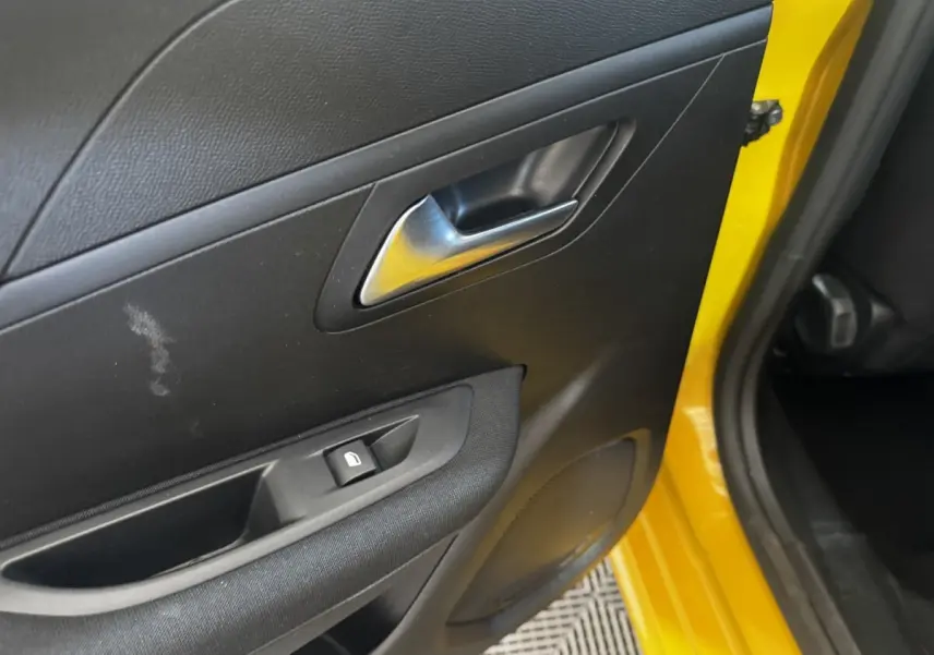 Gros plan sur la porte arrière gauche noire avec poignée argentée et cadre jaune vif de la Peugeot 208 2023.