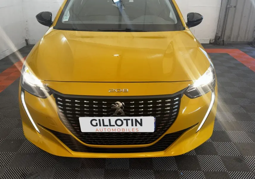 Vue frontale d'une Peugeot 208 jaune avec phares allumés et calandre noire distinctive.