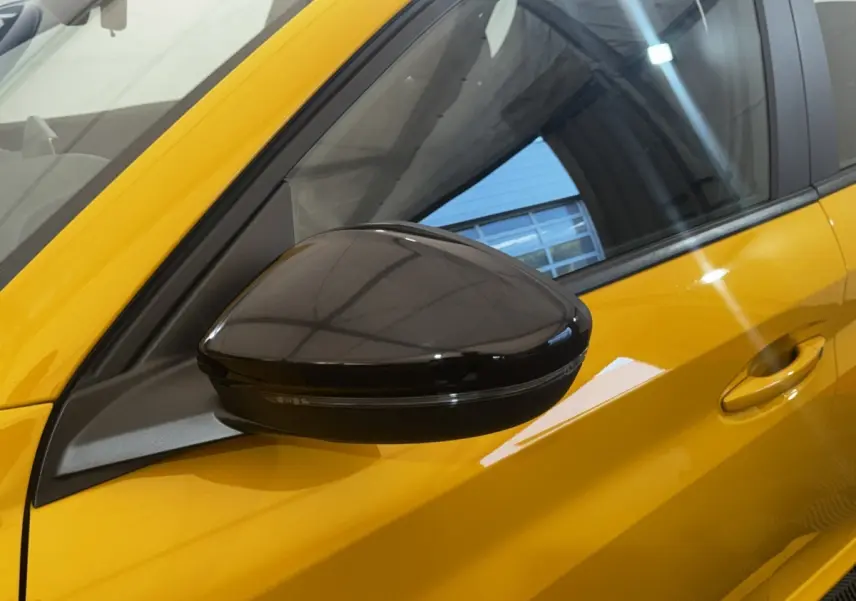 Rétroviseur noir en gros plan côté gauche sur Peugeot 208 jaune vif, avec reflet de l'environnement intérieur.
