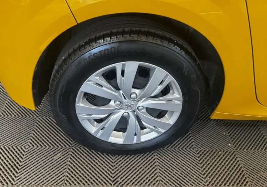 Gros plan sur la roue avant droite d’une Peugeot 208 jaune, jante en alliage argenté avec logo lion au centre.