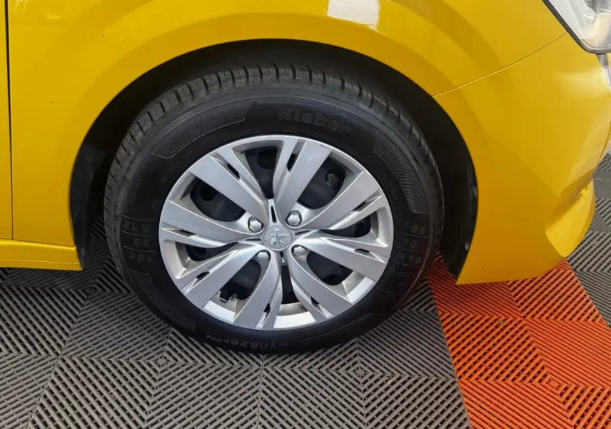 Gros plan sur la roue avant gauche d’une Peugeot 208 jaune 2023 avec jante alliage et pneu Kleber.