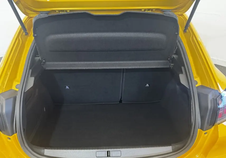 Coffre ouvert vu de l'arrière d'une Peugeot 208 jaune 2023, montrant l'espace de chargement vide et la tablette de séparation.