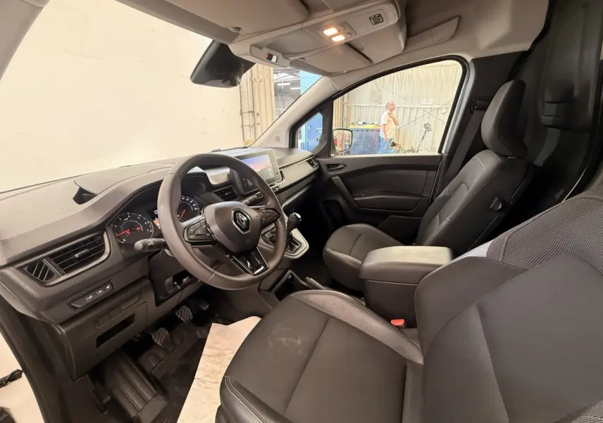 Vue intérieure côté conducteur du Renault Kangoo 2023, volant multifonctions et sièges noirs en tissu et cuir.