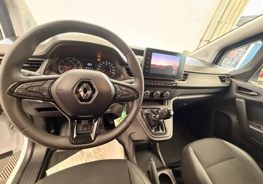 Vue intérieure avant du Renault Kangoo blanc 2023, volant multifonctions et écran tactile central visible.