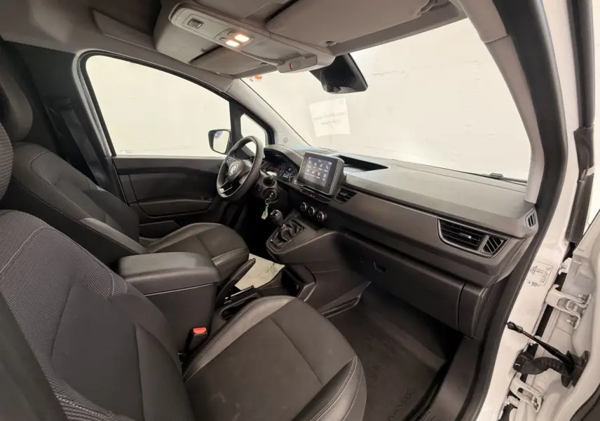 Vue intérieure côté droit du Renault Kangoo blanc 2023, montrant le tableau de bord et les sièges avant noirs.