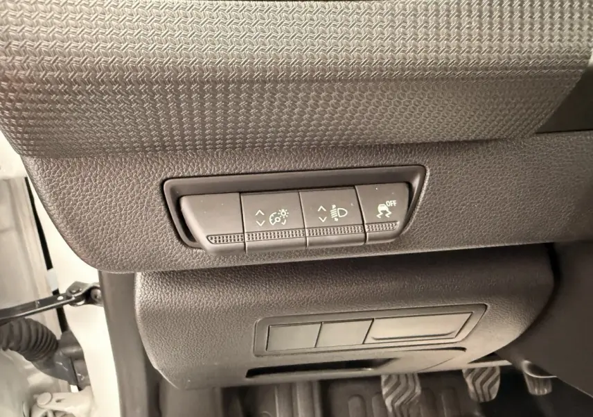 Gros plan sur les commandes de réglage des phares et antipatinage sous le tableau de bord d’un Renault Kangoo blanc.