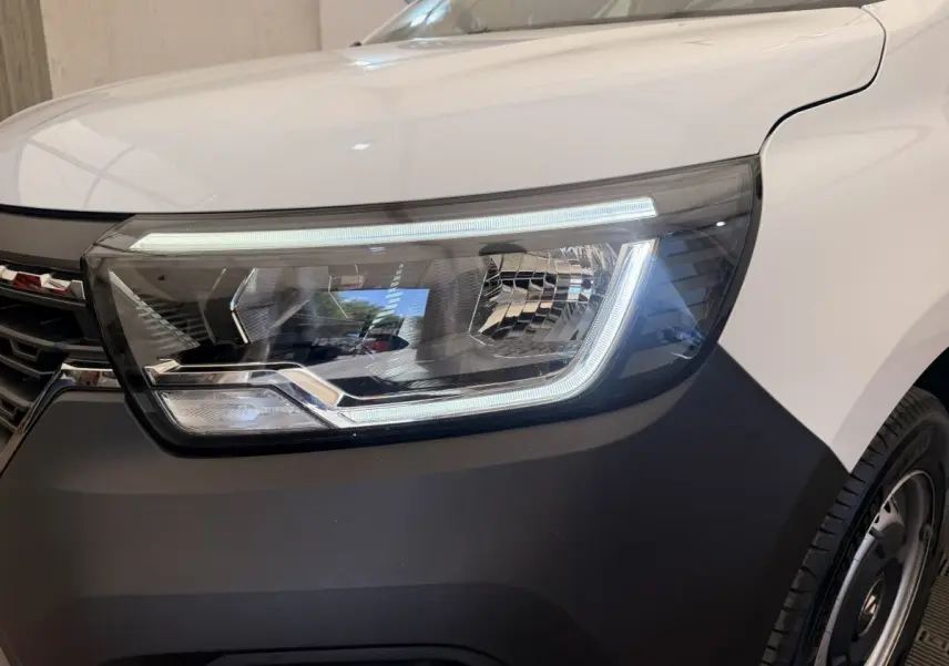 Gros plan sur le phare avant droit du Renault Kangoo blanc 2023 avec éclairage LED et pare-chocs noir mat.