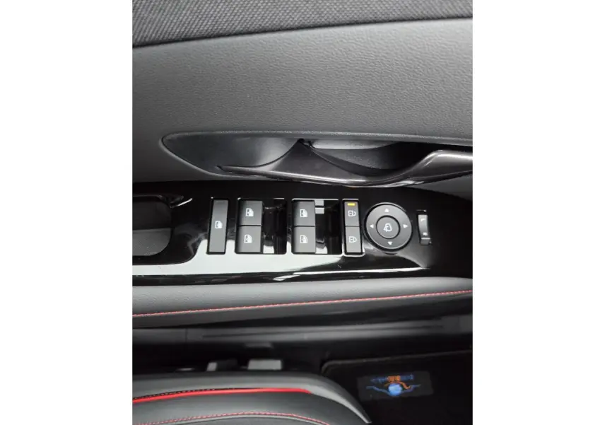 Gros plan sur la commande des vitres et rétroviseurs noirs brillants avec surpiqûres rouges sur la porte côté gauche du Hyundai Tucson 2025.
