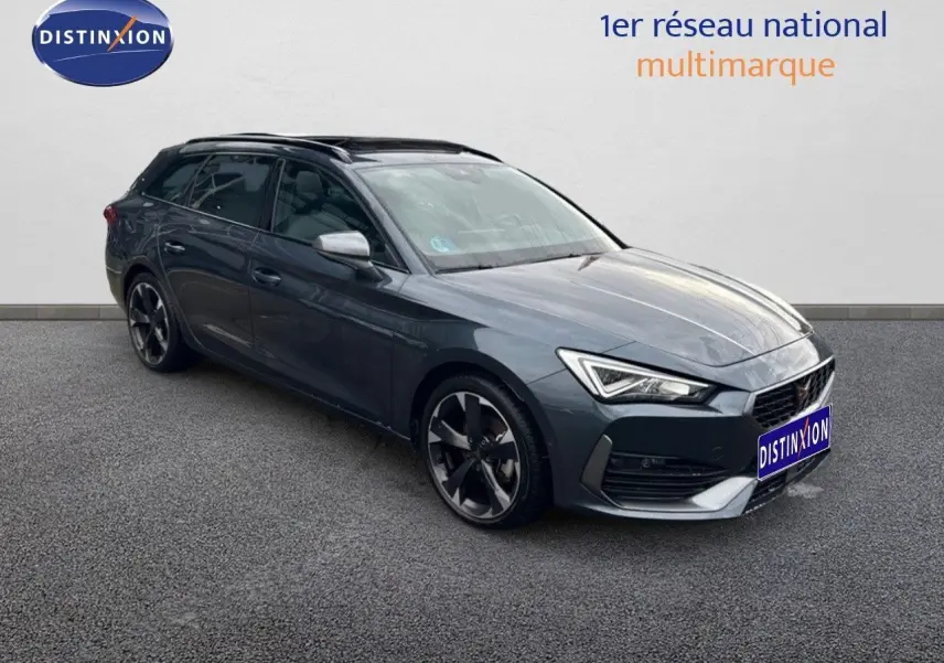 CUPRA Leon ST gris magnétique métal en 3/4 avant droit, avec jantes noires bi-ton et phares LED allumés.