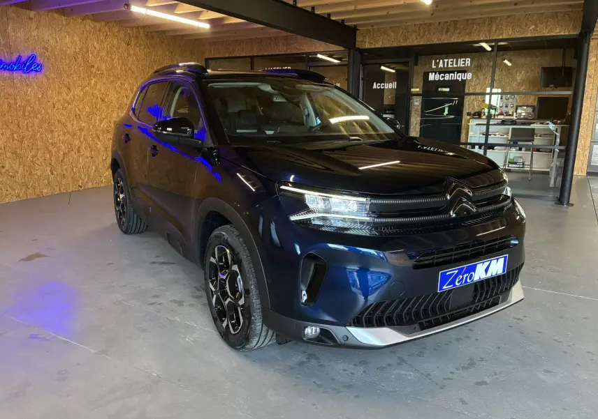 Citroën C5 Aircross bleu Eclipse Metal en 3/4 avant droit, avec jantes noires et éclairage LED visible en intérieur d'atelier.
