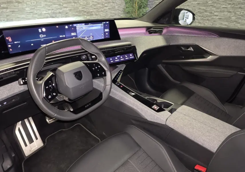 Intérieur Peugeot 3008 GT hybride 2025 vu côté conducteur, tableau de bord gris et noir avec écran panoramique 21 pouces.