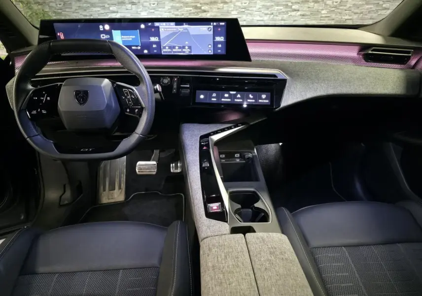 Vue intérieure avant du Peugeot 3008 gris 2025, tableau de bord avec écran panoramique et éclairage d'ambiance violet.