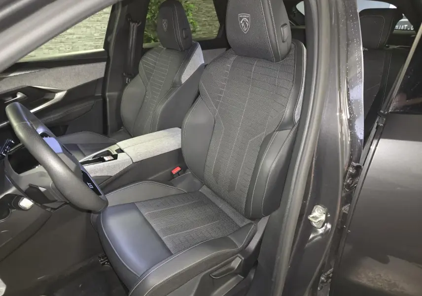 Vue intérieure côté conducteur du Peugeot 3008 gris 2025, sièges tissu et cuir avec logo Peugeot brodé sur appuie-tête.