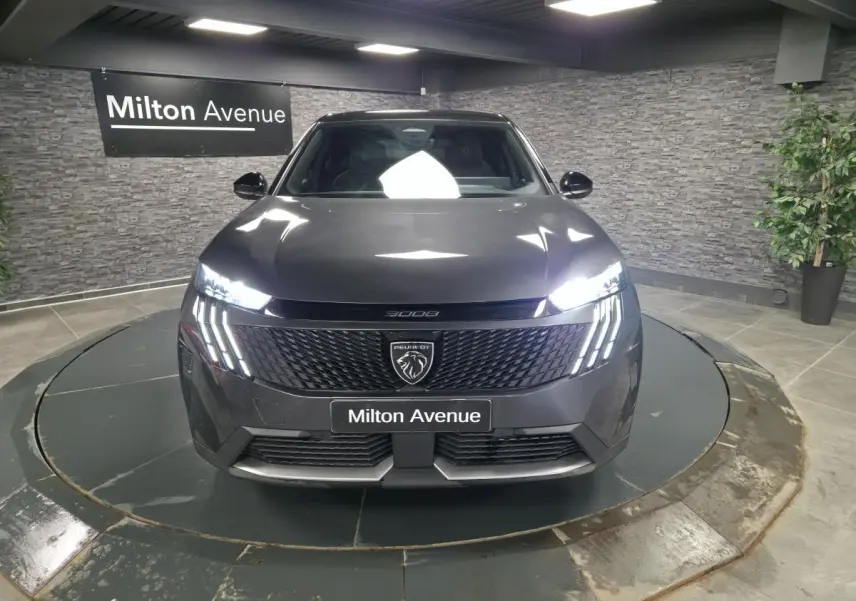 Peugeot 3008 gris vue de face, avec calandre noire et feux LED à griffes allumés dans un showroom.