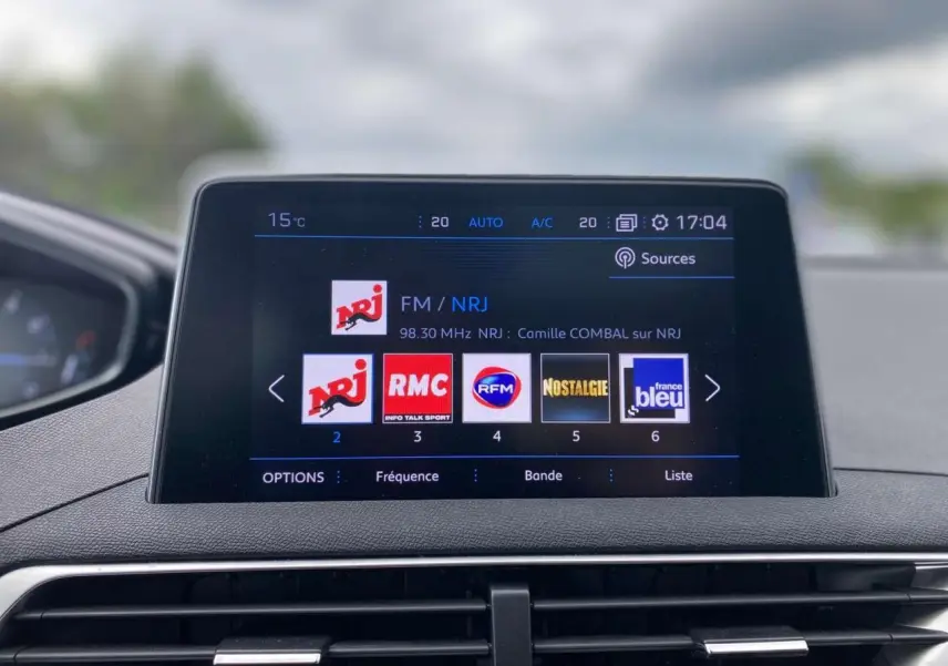 Écran tactile central du Peugeot 3008 blanc 2019 affichant les stations radio avec tableau de bord en arrière-plan flou.