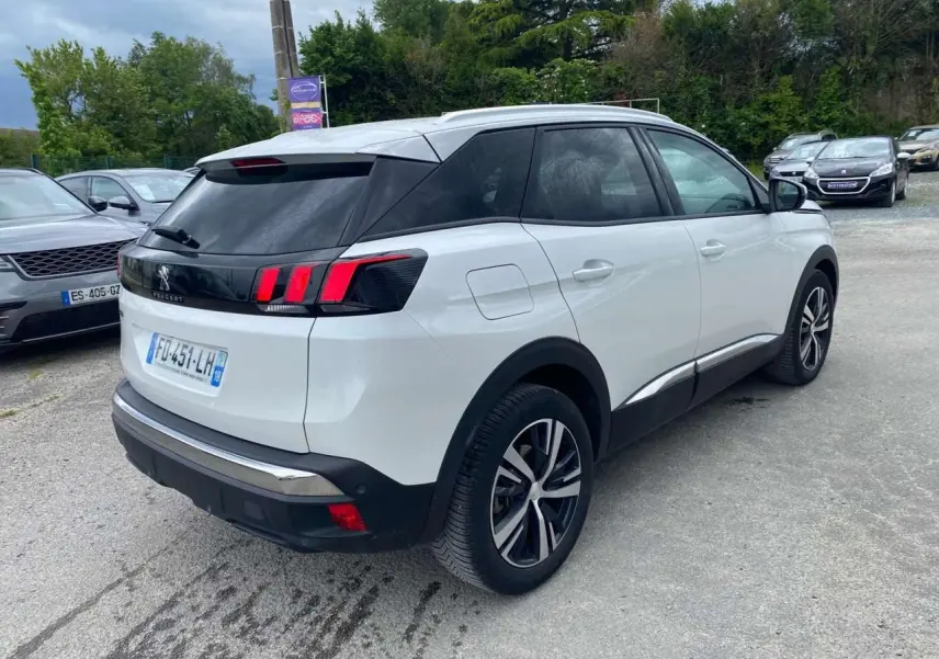 Vue 3/4 arrière droite d’un Peugeot 3008 blanc nacré avec jantes alliage bi-ton et barres de toit profilées en aluminium.