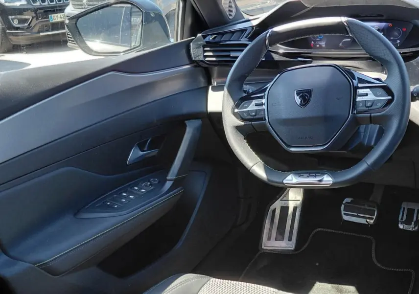Vue intérieure côté conducteur de la Peugeot 308 Hybrid 145 GT 2025, volant cuir GT et cockpit numérique visibles.