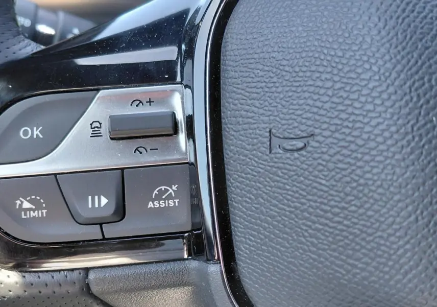 Gros plan sur les commandes du volant cuir perforé de la Peugeot 308 Hybrid 145 e-DCS6 GT, boutons régulateur et limiteur.