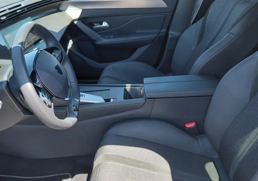 Intérieur avant droit de la Peugeot 308 Hybrid 145 e-DCS6 GT 2025, sièges noirs et volant cuir avec cockpit numérique.