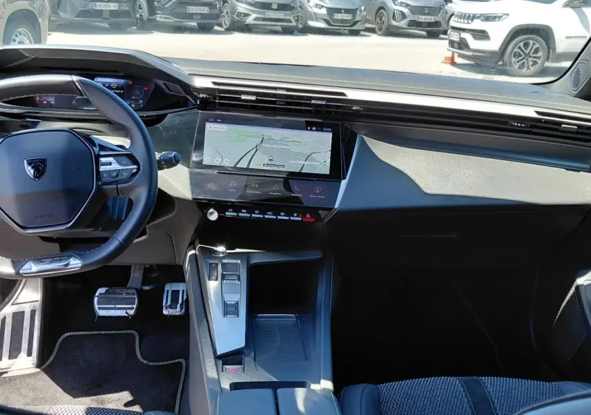 Vue intérieure avant du Peugeot 308 Hybrid 145 e-DCS6 GT gris, avec volant cuir et écran tactile central affichant la navigation.