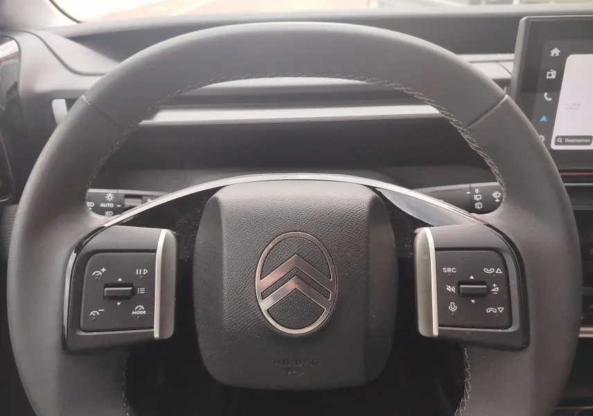 Vue rapprochée du volant noir avec logo Citroën argenté et commandes intégrées du tableau de bord d'une C3 2025.