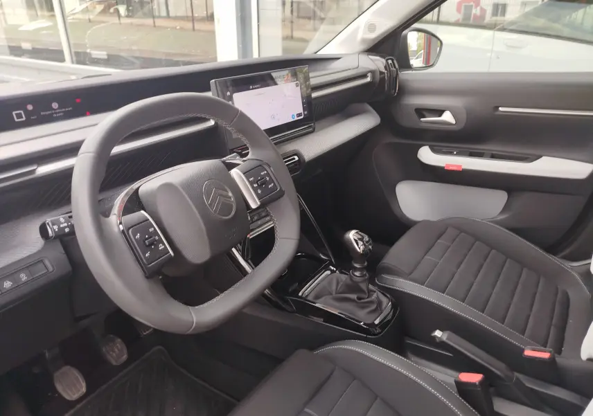 Vue intérieure côté conducteur de la Citroën C3 2025, volant multifonction, écran tactile et sellerie noire avec surpiqûres grises.