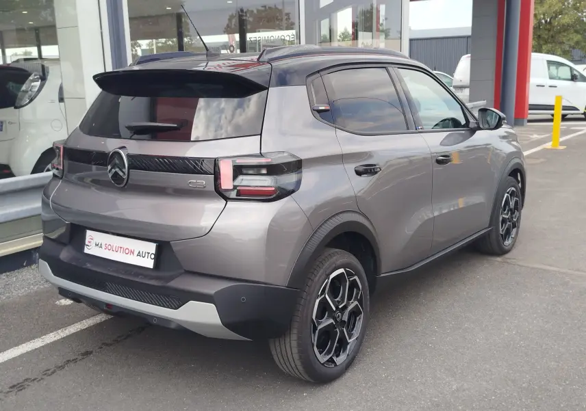 Vue 3/4 arrière droite d'une Citroën C3 gris foncé avec toit noir, jantes bi-ton et feux arrière LED distinctifs.
