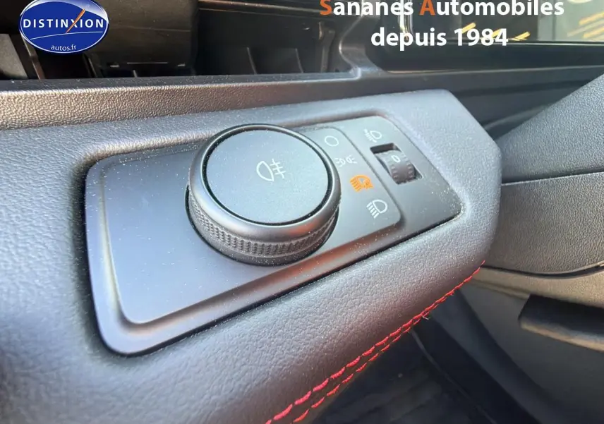 Gros plan sur le bouton de réglage des phares dans l'habitacle du Ford Puma bleu, avec surpiqûres rouges visibles.