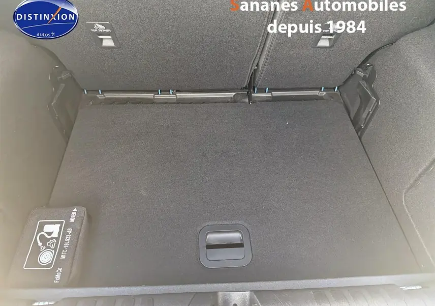 Coffre ouvert d’un Ford Puma bleu, vue de dessus montrant le plancher plat et un kit de réparation pneus rangé sur le côté.