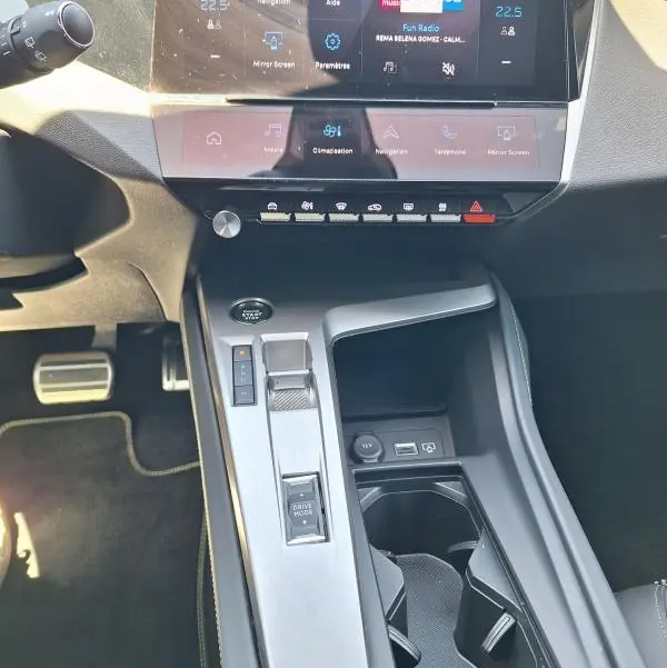 Vue intérieure centrée sur la console centrale et l'écran tactile du Peugeot 308 Hybrid 145 e-DCS6 GT noir de 2025.