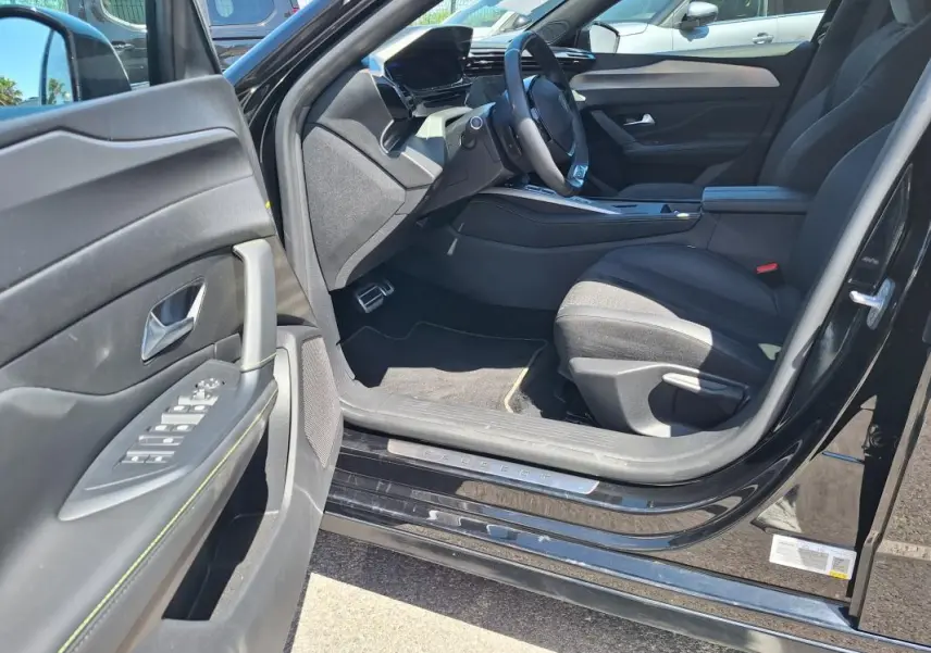 Intérieur côté conducteur de la Peugeot 308 Hybrid 145 GT noir 2025, avec porte ouverte et tableau de bord moderne.