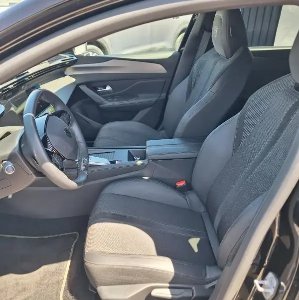 Intérieur avant droit de la Peugeot 308 Hybrid 145 GT 2025 noire, sièges tissu et cuir avec accoudoir central.