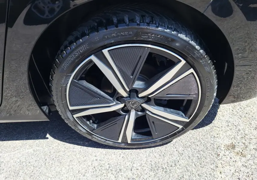 Gros plan sur la jante alliage 18 pouces noire et argentée d'une Peugeot 308 Hybrid 145 e-DCS6 GT noire.