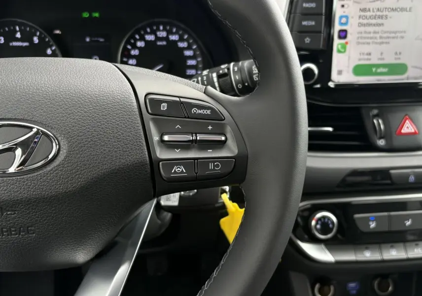 Gros plan sur le volant cuir côté gauche et tableau de bord avec écran tactile affichant Apple CarPlay dans une Hyundai i30 SW gris argent 2025.