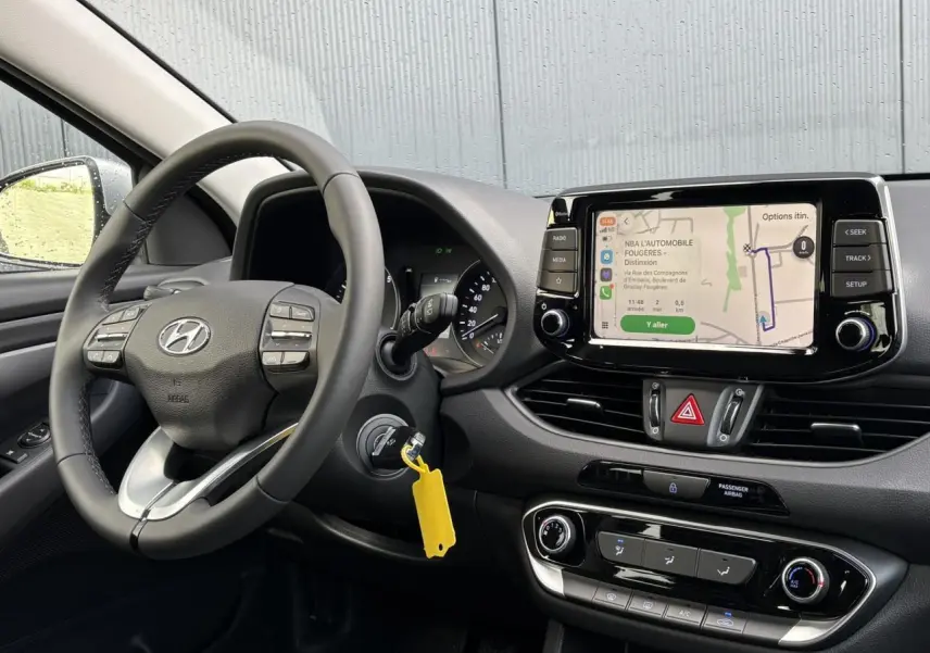 Vue intérieure côté conducteur du tableau de bord gris avec volant cuir et écran tactile affichant la navigation.