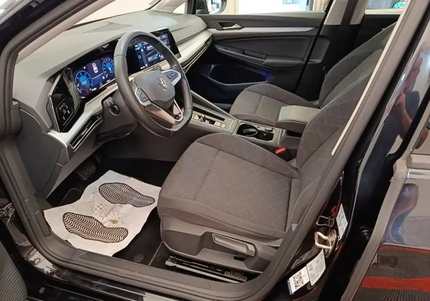 Vue intérieure côté conducteur de la Volkswagen Golf noire 2023, avec tableau de bord digital et sièges tissu gris.
