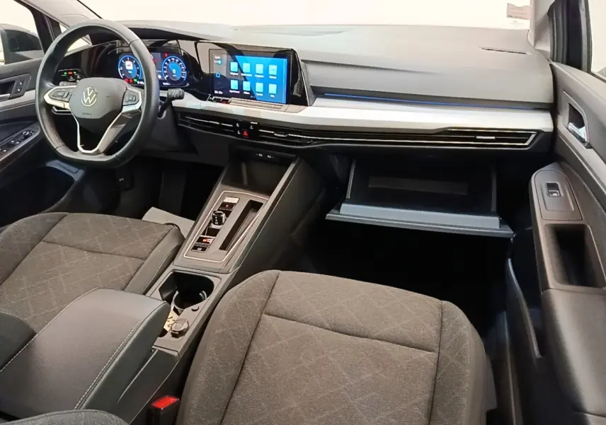 Intérieur avant de la Volkswagen Golf 2023, vue côté passager, tableau de bord noir avec écran tactile et volant cuir.