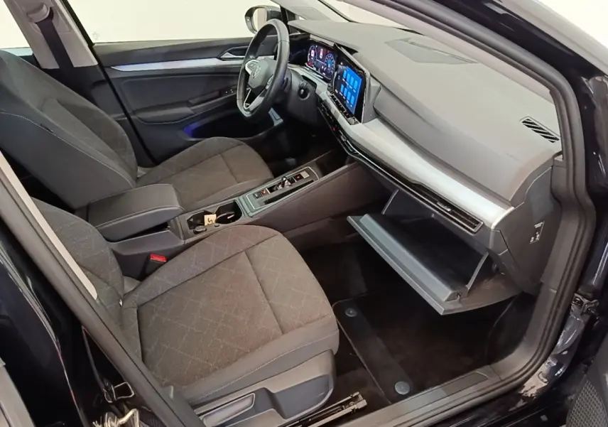 Vue intérieure côté passager de la Volkswagen Golf noire 2023, tableau de bord numérique et boîte à gants ouverte.