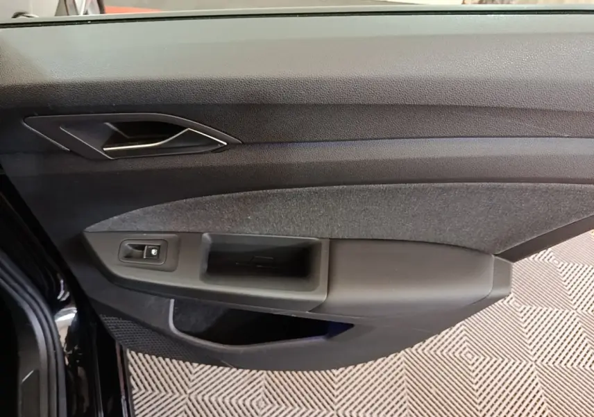 Vue rapprochée de la porte avant gauche noire de la Volkswagen Golf 2023, avec poignée et commande de vitre.