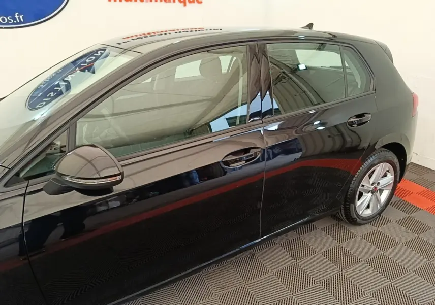 Profil côté gauche d'une Volkswagen Golf noire 2023, avec rétroviseur et jante alliage visibles sur sol intérieur.