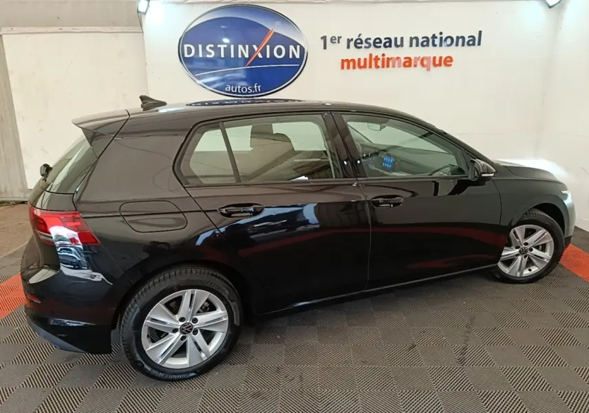 Profil droit d'une Volkswagen Golf noire 2023 dans un showroom avec jantes alliage et vitres teintées.
