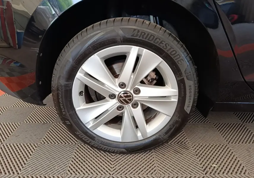 Gros plan sur la roue avant gauche d'une Volkswagen Golf noire, jante alliage argentée avec logo VW central.