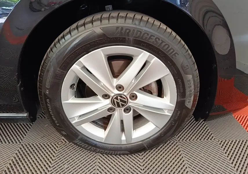 Gros plan sur la roue avant droite d'une Volkswagen Golf noire, jante alliage argentée avec logo VW central.