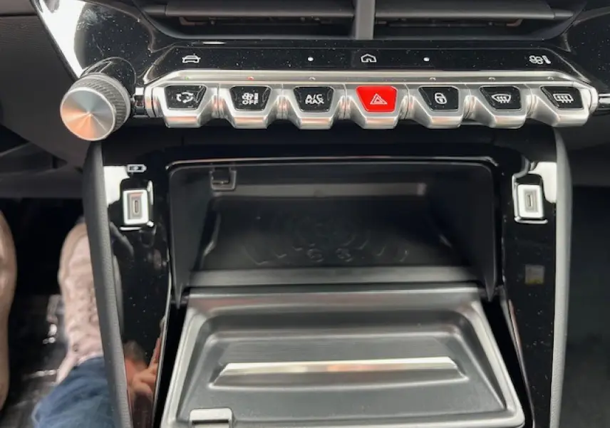 Gros plan sur la console centrale du Peugeot 2008 2026, montrant les boutons de commande et le chargeur smartphone à induction.