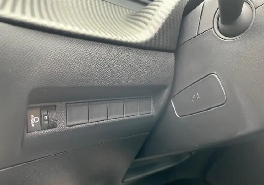 Détail intérieur côté gauche du tableau de bord du Peugeot 2008 2026 avec commandes d’éclairage et texture carbone.