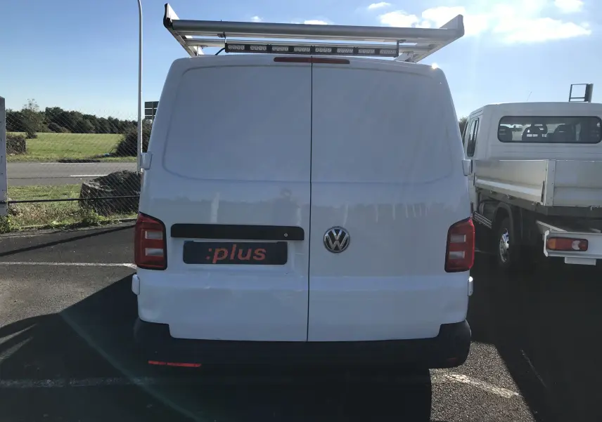 Vue arrière d'un Volkswagen Transporter T6 blanc avec porte arrière double et galerie de toit métallique.