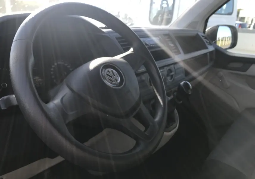 Intérieur du Volkswagen Transporter T6 blanc, vue sur le volant, tableau de bord et levier de vitesse manuel côté conducteur.