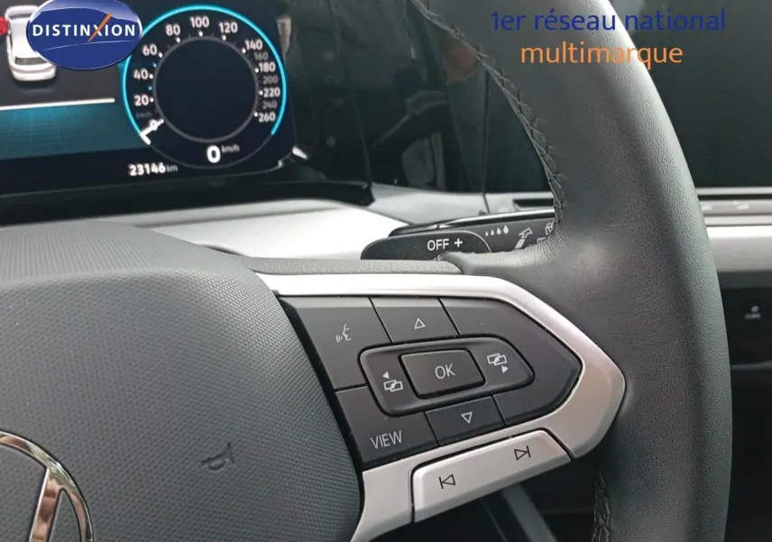 Gros plan sur le volant noir de la Volkswagen Golf VIII avec commandes multifonctions et tableau de bord numérique en arrière-plan.