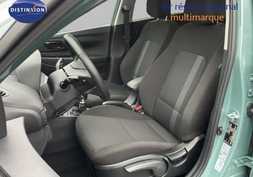 Vue intérieure côté conducteur de la Hyundai i20 2025 vert mangrove, sièges tissu noir et volant multifonction.